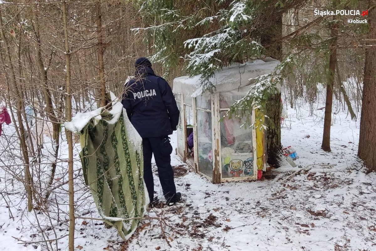 Bezdomna kobieta siedzi w prowizorycznym schronieniu, obok stoi umundurowany policjant