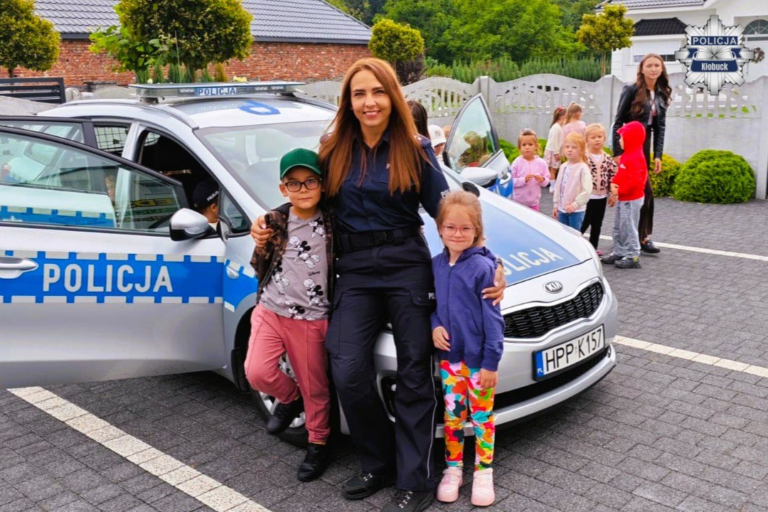 policjantka stoi z dziećmi przy radiowozie