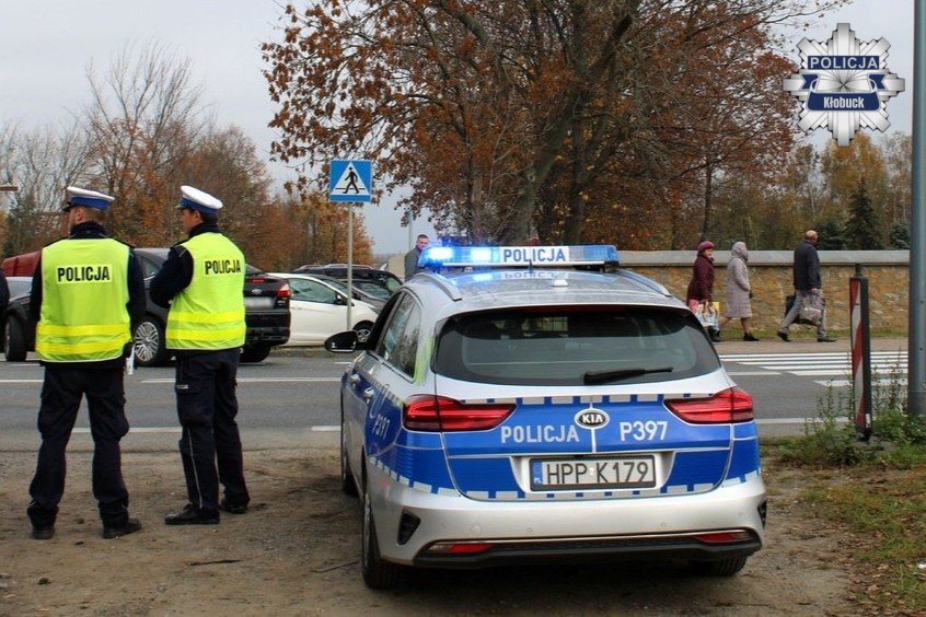 dwóch umundurowanych policjantów stoi przy radiowozie