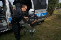 Dzieci przymierzają policyjną kamizelkę przeciwuderzeniową, kask i tarczę.