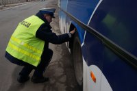 Policjant sprawdza stan opon w autobusie.
