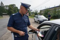 Policjant wręcza kierowcy ulotki.