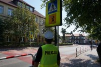 Policjant sprawdza oznakowanie przejścia dla pieszych przy szkole.
