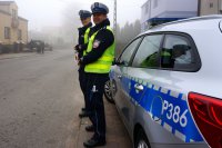 Policjanci stoją przy radiowozie na drodze.