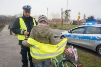 Policjant wręcza kamizelkę odblaskową.