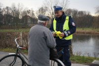 Policjant wręcza kamizelkę odblaskową.