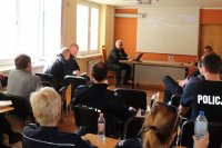 Zdjęcie kolorowe. Sala konferencyjna, kilkunastu policjantów słucha prelekcji powiatowego lekarza weterynarii.