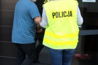 policjantka prowadzi zatrzymanego, który ma założone na rekach kajdanki