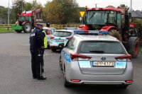 policjanci stoją obok radiowozu, w tle ciągniki rolnicze