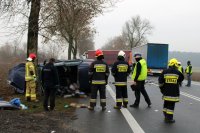 fotografia przedstawia policjantów i strażaków wykonujących czynności na miejscu zdarzenia oraz pojazdy, które brały udział w zdarzeniu: rozbity ford i volvo,a także inny pojazd ciężarowy, który nie uczestniczył w zdarzeniu