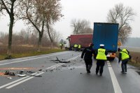 fotografia przedstawia policjantów przeprowadzających oględziny na tle dwóch pojazdów ciężarowych, w tym rozbitego volvo