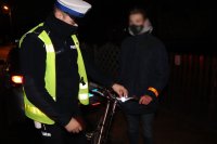 policjant ruchu drogowego zakłada odblask na kierownicę rowerzyście który stoi obok roweru