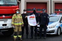 dwóch strażaków i dwóch policjantów na tle radiowozu policyjnego i wozu strażackiego