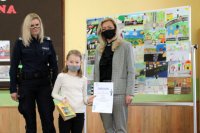 dziewczynka z dyplomem stoi wspólnie z policjantką i dyrektorką szkoły