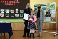 dziewczynka z dyplomem stoi wspólnie z policjantką i dyrektorem szkoły