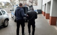 policjant kryminalny prowadzący mężczyznę w kajdankach do radiowozu