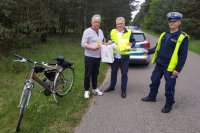 policjant ruchu drogowego, pracownik urzędu gminy i rowerzysta trzymający odblaski