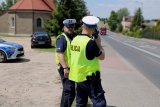 umundurowaniu policjanci stoją przy drodze, jeden kontroluje prędkość