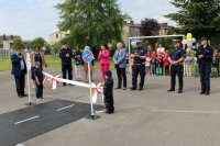 umundurowani policjanci wraz z innymi osobami oraz przedszkolakami stoją przy mobilnym miasteczku ruchu drogowego
