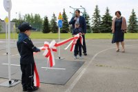 dzieci przebrane za policjanta trzymają biało czerwoną wstęgę, w tle stoi mężczyzna z mikrofonem oraz kobieta