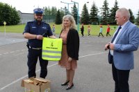 umundurowany policjant trzyma kamizelkę odblaskową, obok stoją mężczyzna i kobieta