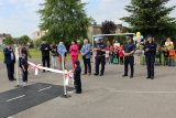 umundurowani policjanci wraz z innymi osobami oraz przedszkolakami stoją przy mobilnym miasteczku ruchu drogowego