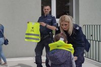 policjantka zakłada dziecku kamizelkę odblaskową, obok stoi policjant, który trzyma kamizelkę w rękach