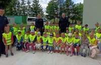 Na zdjęciu widać dwóch policjantów i policjantkę oraz grupę dzieci w kamizelkach odblaskowych
