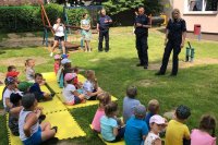 policjant i policjantka stoją przodem na zdjęciu, rozmawiają z dziećmi, które siedzą przodem do nich na matach