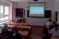 umundurowana policjantka siedzi w klasie siedzi za biurkiem przodem do uczniów. którzy siedzą w ławkach