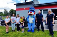 umundurowani policjanci stoją przodem do zdjęcia wraz z policyjną maskotką i dziećmi