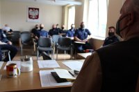 na zdjęciu widać umundurowanych policjantów siedzących na krzesełkach przodem do zdjęcia oraz funkcjonariusza Państwowej Straży Rybackiej, który siedzi tyłem do zdjęcia