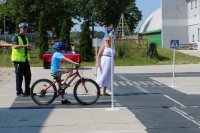 na zdjęciu widać chłopaka, który siedzi na rowerze, ma kask na głowie, po lewej stronie stoi policjant a po prawej nauczycielka