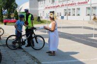 na zdjęciu widać chłopaka, który ma założony kask na głowę, trzyma rower, przy nim stoi umundurowany policjant, który ręką trzyma rower,  a obok nauczycielka