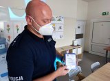 umundurowany policjant w maseczce prezentuje ulotki profilaktyczne