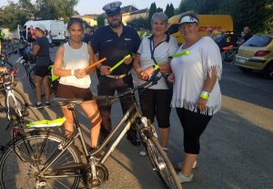 policjant ruchu drogowego stoi z cyklistami trzymającymi opaski odblaskowe