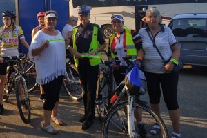policjantka ruchu drogowego stoi z cyklistami mającymi opaski odblaskowe