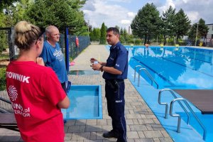 umundurowany policjant podczas rozmowy z ratownikami, w tle basen