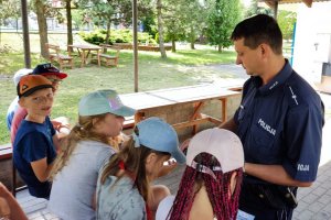 umundurowany policjant rozdaje ulotki dzieciom