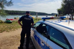 umundurowany policjant stoi przy radiowozie w tle zbiornik wodny