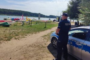 umundurowany policjant stoi przy radiowozie w tle zbiornik wodny