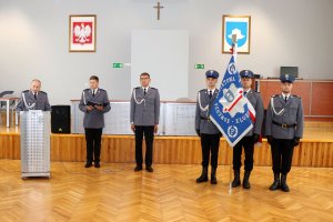 policjant w mundurze galowym stoi przy mównicy, z prawej strony sztandar