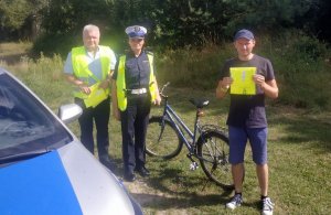 policjantka w mundurze stoi z rowerzystą, który w rękach trzymają kamizelkę odblaskową