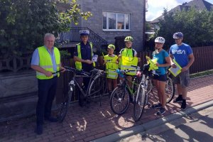 umundurowana policjantka stoi na chodniku wraz z rowerzystami, którzy trzymają w rękach elementy odblaskowe