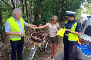 mężczyzna w kamizelce odblaskowej rozdaje elementy odblaskowe rowerzystce, obok stoi umundurowana policjantka