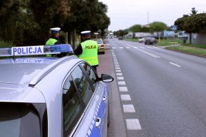 policjanci stoją przy radiowozie, jeden mierzy prędkość