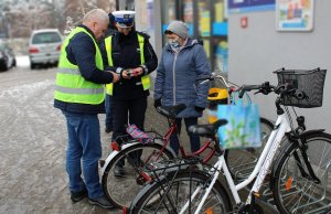 Policjanci oraz mężczyzna w kamizelce odblaskowej przekazują odblaski rowerzystce