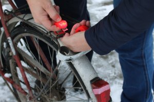 Mężczyzna w kamizelce montuje czerwoną lampkę do roweru