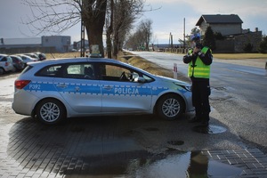 policjant stoi przy oznakowanym radiowozie i kontroluje prędkość
