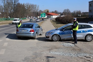 Na zdjęciu widać oznakowany radiowóz przy którym stoi policjant, obok inny policjant rozmawia z kierowcą forda, który popełnił wykroczenie